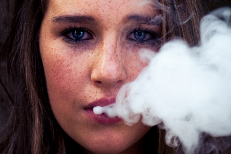 Girl with freckles and blue eyes exhaling smoke