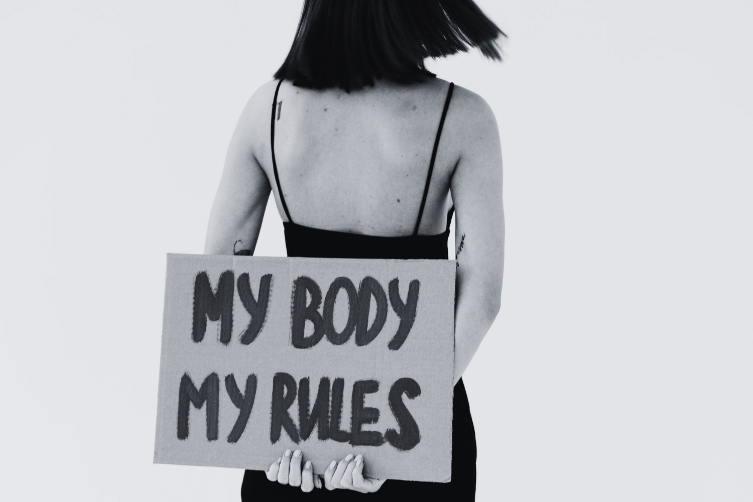 Back view of a woman holding a placard about 'My body, my rules'