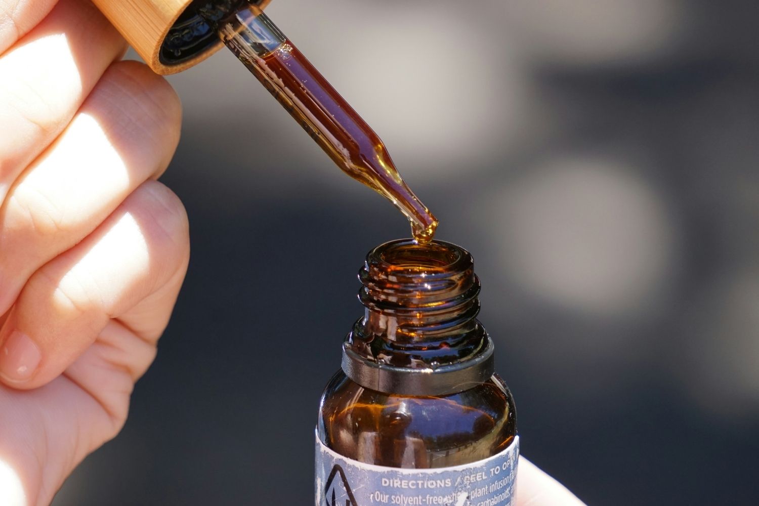 Image of someone using a dropped of CBD oil into a brown bottle.