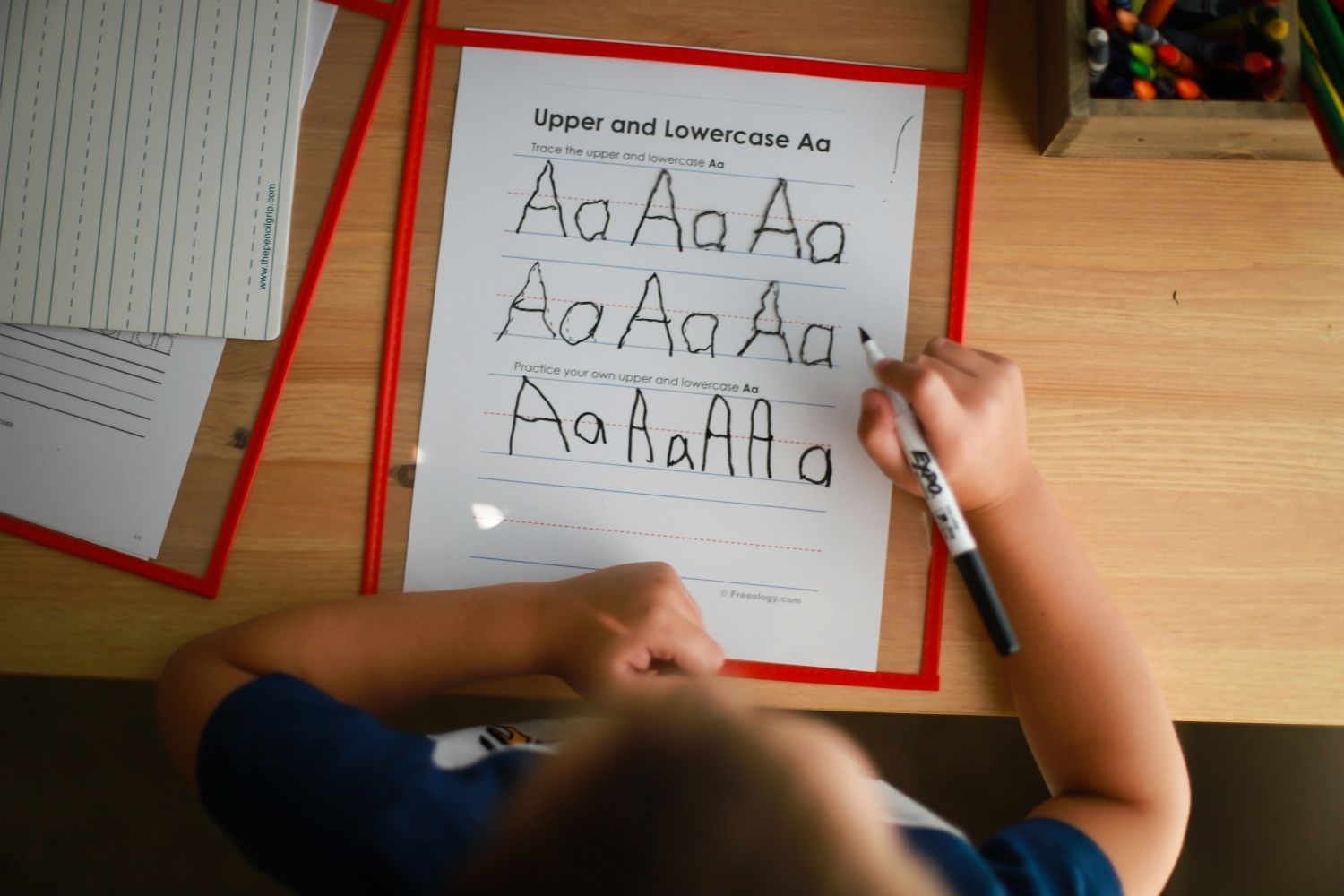 Child practising writing out capital and lowercase 'A's on a worksheet.