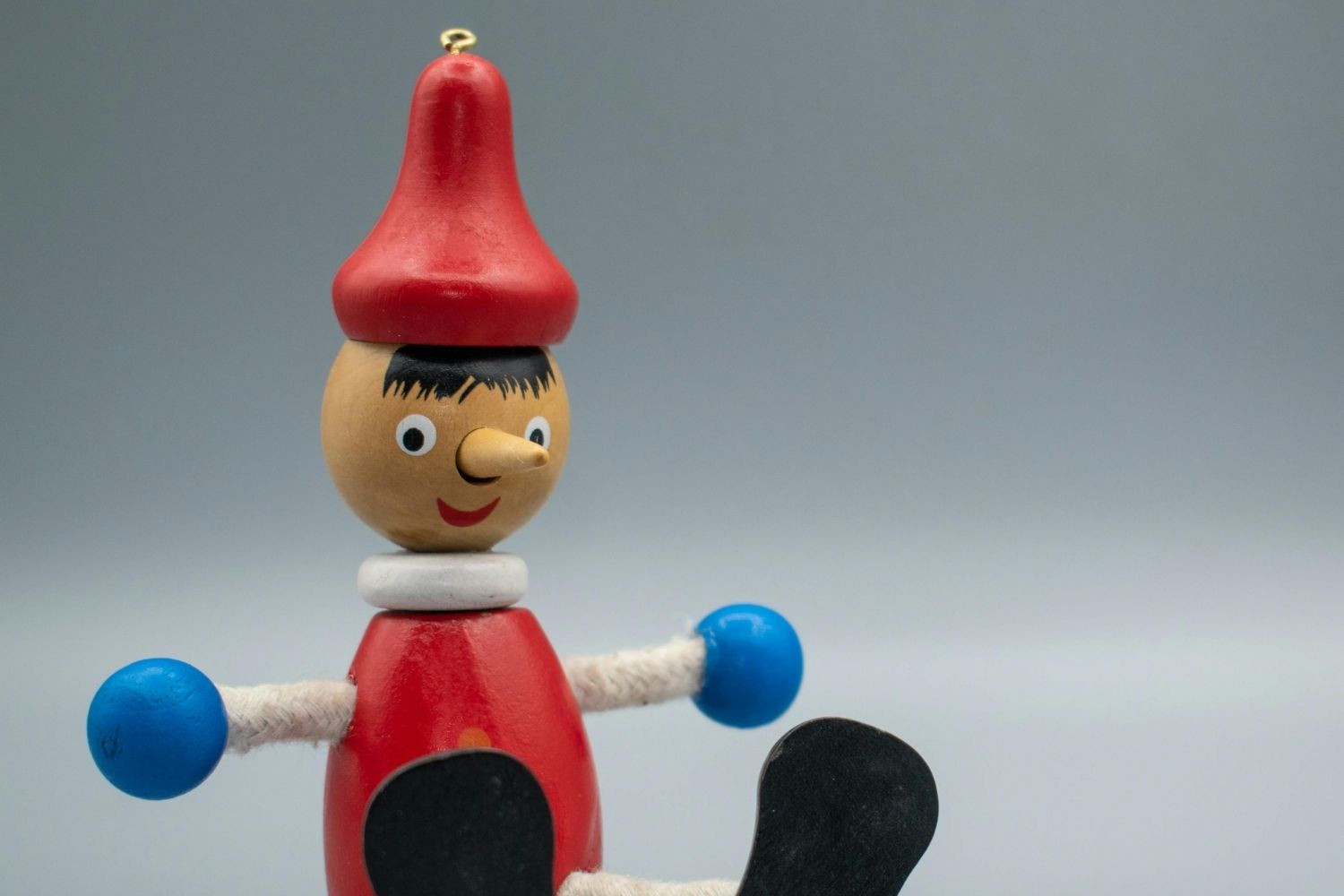 Wooden puppet with a long wooden nose in a red hat, red shirt, white sleeves, and blue gloves.