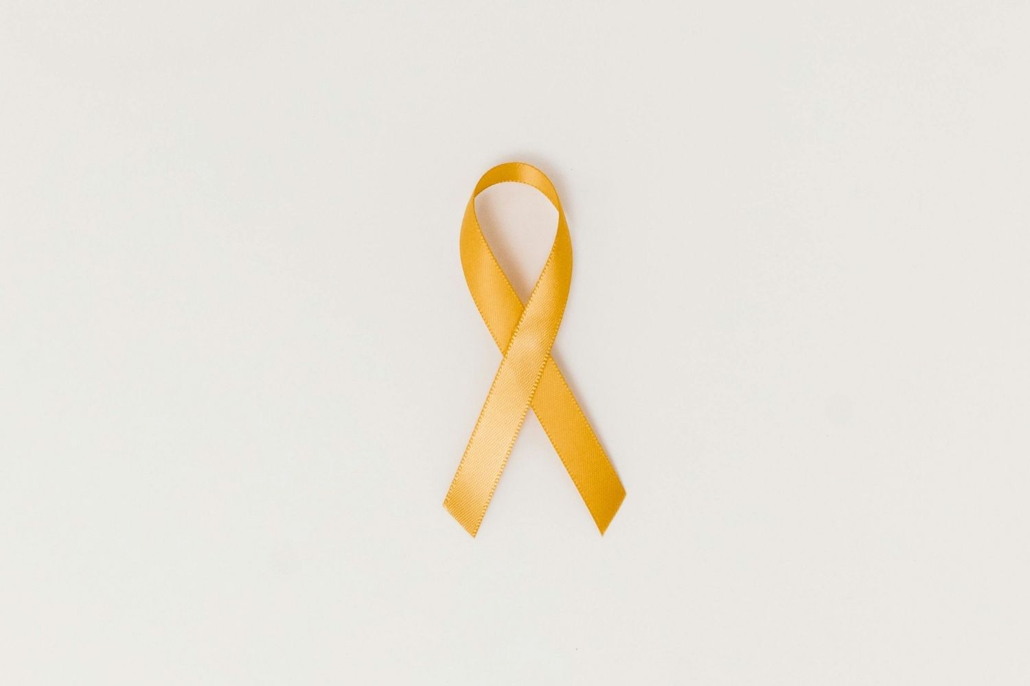 Yellow ribbon crossed over on in the middle using the other side o the ribbon. It sits on a white background for suicide awareness.