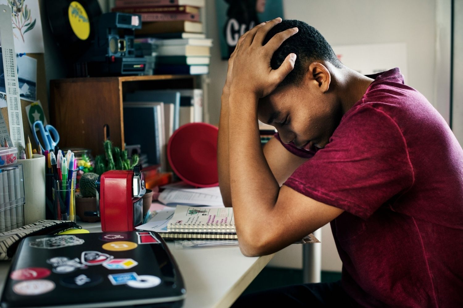 Young black student sits with their head in their hands as they look at their schoolwork on their desk.