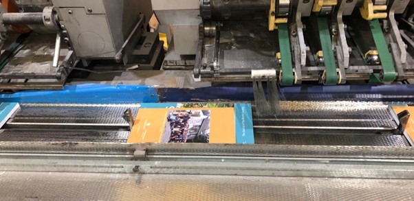 Photograph of a printed journal and insert on a production line ready to be wrapped in paper for mailing