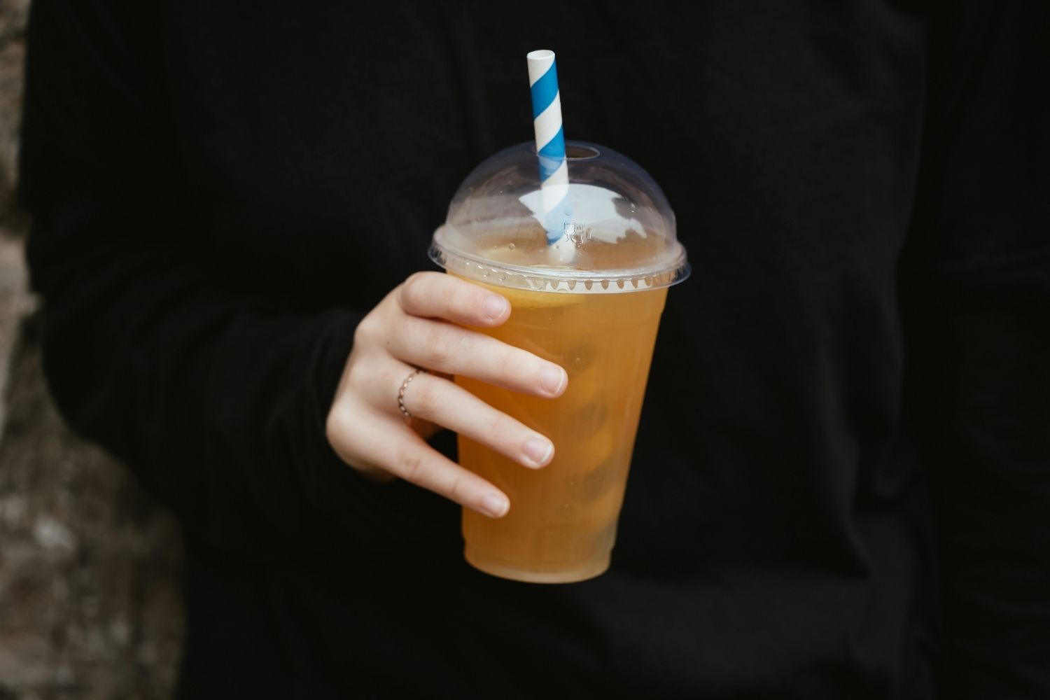 Image of someone holding a plastic takeaway cup of an iced drink with a plastic straw in it.