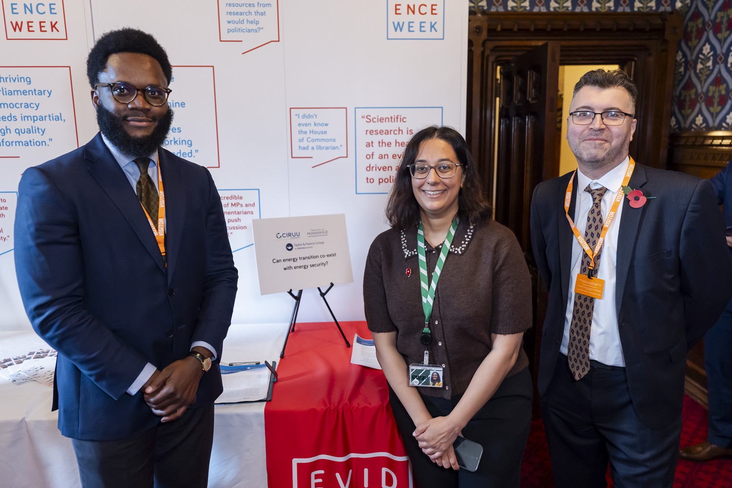 Three smiling people standing in front of a display table. Sign on the table reads "Can energy security transition co-exist with energy security?'