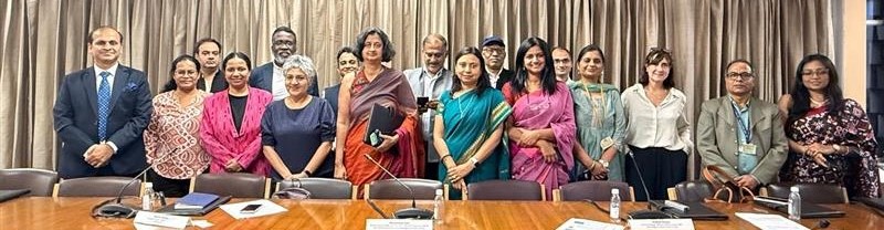 A group of 17 people standing together to pose for the photo behind a long conference table.