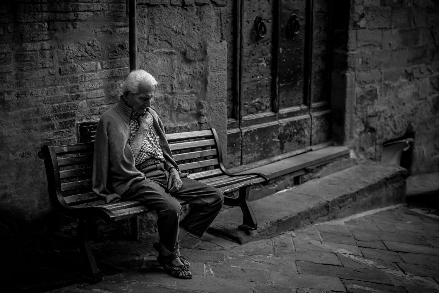A solitary man sits on a bench. The photo is treated with a black and white filter.