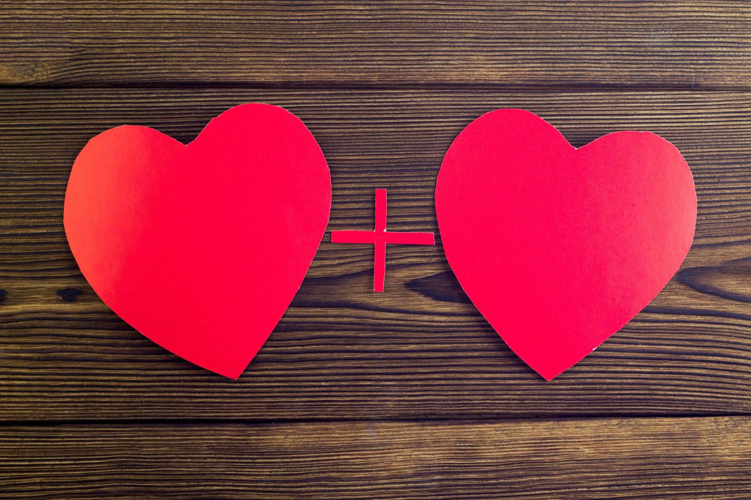 Two red paper hearts sit on top of a dark wooden background.